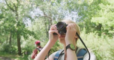 Sırt çantalı mutlu çift parkta fotoğraf çekiyor, ağır çekimde. Doğa, yürüyüş ve park konsepti.