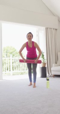 Asyalı kadının yoga minderini yavaş çekimde yatak odasına koyduğu dikey video. Kaliteli zaman, yaşam tarzı ve ev hayatı kavramı harcamak.