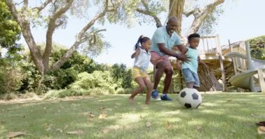 Torunları bahçede yavaş çekimde futbol oynayan mutlu Afro-Amerikan büyükbabaları. Ev kavramında kaliteli zaman geçirmek.