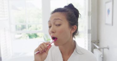 Mutlu Asyalı kadın banyoda dişlerini fırçalıyor, ağır çekimde. Kaliteli zaman, yaşam tarzı ve ev hayatı kavramı harcamak.