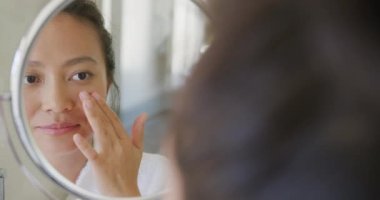 Mutlu Asyalı kadın aynaya bakıyor ve banyoda yüzüne dokunuyor, ağır çekimde. Kaliteli zaman, yaşam tarzı ve ev hayatı kavramı harcamak.