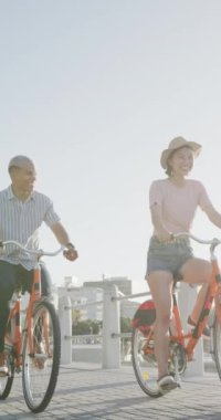 Melez çiftlerin gezinti güvertesinde ağır çekimde bisiklet sürüşlerinin dikey videosu. Kaliteli zaman, yaşam tarzı ve tatil konsepti harcamak.