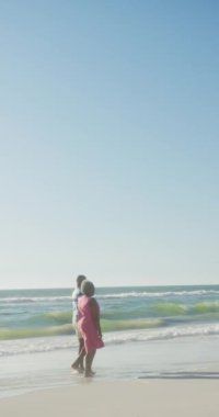 Ağır çekimde sahilde yürüyen yaşlı Afrikalı Amerikalı bir çiftin dikey videosu. Kaliteli zaman, yaşam tarzı, emeklilik ve tatil konsepti.