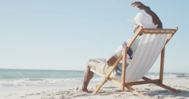 Sahildeki güverte koltuğunda oturan kıdemli Afro-Amerikan adam yavaş çekimde fotokopi çekiyor. Kaliteli zaman geçirmek, yaşam tarzı, emeklilik ve tatil kavramı.