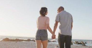 Sahilde yürüyen ve el ele tutuşan mutlu çift, ağır çekimde. Romantizm, birliktelik, doğa ve tatil kavramı.