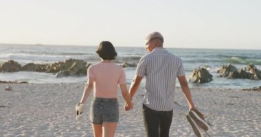 Sahilde yürüyen ve el ele tutuşan mutlu çift, ağır çekimde. Romantizm, birliktelik, doğa ve tatil kavramı.