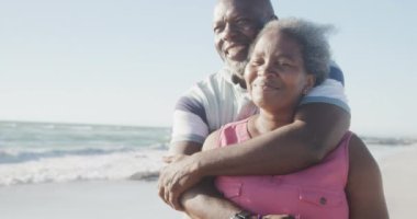 Mutlu Afrika kökenli Amerikalı çiftler kumsalda kucaklaşıyorlar, ağır çekimde. Kaliteli zaman geçirmek, yaşam tarzı, emeklilik ve tatil kavramı.