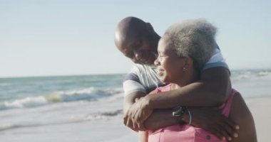 Mutlu Afrika kökenli Amerikalı çiftler kumsalda kucaklaşıyorlar, ağır çekimde. Kaliteli zaman geçirmek, yaşam tarzı, emeklilik ve tatil kavramı.