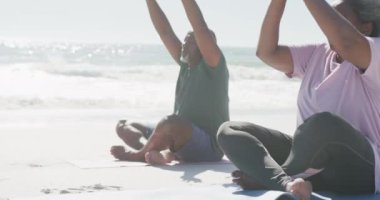 Mutlu Afrika kökenli Amerikalı çift yavaş çekimde yoga yapıyor ve plajda meditasyon yapıyor. Kaliteli zaman geçirmek, yaşam tarzı, emeklilik ve tatil kavramı.
