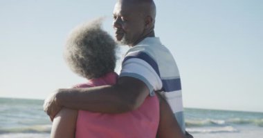 Mutlu kıdemli Afro-Amerikan çiftler kumsalda yürüyor ve sarılıyorlar, ağır çekimde. Kaliteli zaman geçirmek, yaşam tarzı, emeklilik ve tatil kavramı.