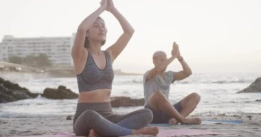 Çift ırklı mutlu çift gün batımında yoga yapıyor ve plajda yavaş çekimde meditasyon yapıyor. Sağlıklı yaşam tarzı, birliktelik, doğa ve tatil kavramı.