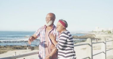 Mutlu kıdemli Afro-Amerikan çifti deniz kenarında geziniyor, ağır çekimde. Kaliteli zaman, yaşam tarzı, tatil ve emeklilik.
