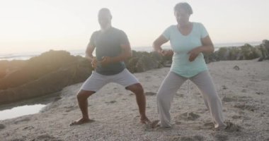 Mutlu Afrika kökenli Amerikalı çift yoga yapıyor, plajda geriniyor, ağır çekimde. Kaliteli zaman, yaşam tarzı, tatil ve emeklilik.