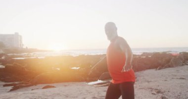 Kıdemli Afro-Amerikan adam yoga yapıyor ve plajda geriniyor, ağır çekimde. Kaliteli zaman, yaşam tarzı, tatil ve emeklilik.