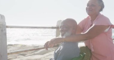 Mutlu kıdemli Afro-Amerikan çifti deniz kenarında geziniyor, ağır çekimde. Kaliteli zaman, yaşam tarzı, tatil ve emeklilik.