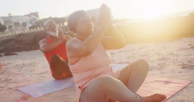Mutlu Afrika kökenli Amerikalı çift yoga yapıyor, plajda meditasyon yapıyor, ağır çekimde. Kaliteli zaman, yaşam tarzı, tatil ve emeklilik.