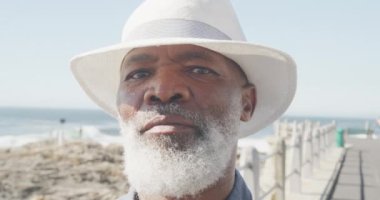 Deniz kenarında gezinen yaşlı Afro-Amerikan bir adamın portresi, ağır çekimde. Kaliteli zaman, yaşam tarzı, tatil ve emeklilik.
