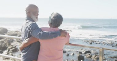 Mutlu kıdemli Afro-Amerikan çifti deniz kenarında geziniyor, ağır çekimde. Kaliteli zaman, yaşam tarzı, tatil ve emeklilik.