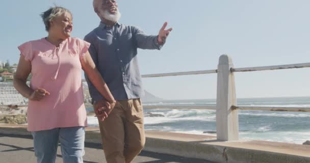 海沿いの遊歩道を歩く幸せなシニアアフリカ系アメリカ人のカップル スローモーション 質の高い時間 ライフスタイル 退職を過ごす — ストック動画