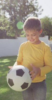 Bahçede futbol oynayan beyaz bir çocuğun portresinin dikey videosu, ağır çekimde. Kaliteli zaman geçirme, ev hayatı ve çocukluk kavramı.