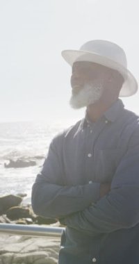 Deniz kenarında gezinen yaşlı Afro-Amerikan bir adamın portresinin dikey videosu, yavaş çekim. Kaliteli zaman, yaşam tarzı, tatil ve emeklilik kavramı.