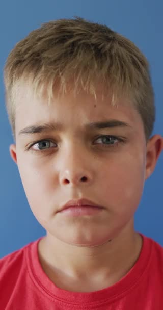 Vídeo Vertical Menino Caucasiano Triste Olhando Para Câmera Fundo Azul — Vídeo de Stock