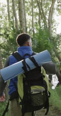 Ormanda yürüyüş yapan melez bir adamın dikey videosu, yavaş çekim. Kaliteli zaman geçirme, yaşam tarzı, doğa, yürüyüş ve kamp konsepti.