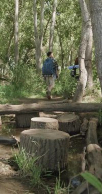 Çift ırklı bir çiftin sırt çantası giyip ormanda yürüyüş yaptığı dikey bir video. Kaliteli zaman geçirme, yaşam tarzı, doğa, yürüyüş ve kamp konsepti.