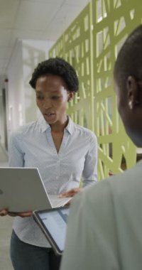 Yavaş çekimde dizüstü bilgisayar kullanan mutlu Afro-Amerikan iş kadınlarının dikey videosu. Küresel iş, finans ve ofis kavramı.