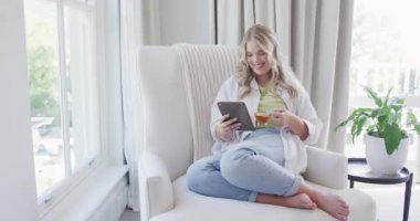 Kafkasyalı mutlu kadın tablet kullanıyor ve yavaş çekimde çay içiyor. Yaşam tarzı, evde kaliteli zaman geçirme ve vücut kapsamı.