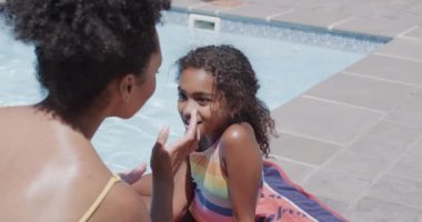 Mutlu Afro-Amerikan anne ve kızı yüzme havuzuyla güneş kremi sürüyor, ağır çekimde. Evde, evde ve ailede kaliteli zaman geçirmek.