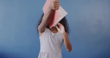 Mutlu Afro-Amerikalı kız elinde mavi arka plan üzerine kitap tutuyor, ağır çekimde. Eğitim, öğrenme ve çocukluk.