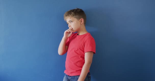 Nachdenklicher Kaukasischer Junge Der Sein Kinn Auf Blauem Hintergrund Hält — Stockvideo