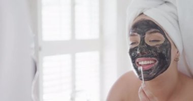 Kafasında havlu olan Kafkas 'lı mutlu kadın yavaş çekimde maske yapıyor. Yaşam tarzı, evde kaliteli zaman geçirme ve vücut kapsamı.