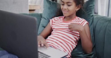 Mutlu Afro-Amerikalı kız kanepede oturuyor, dizüstü bilgisayar kullanıyor, ağır çekimde. Evde, evde ve çocuklukta kaliteli zaman geçirmek.