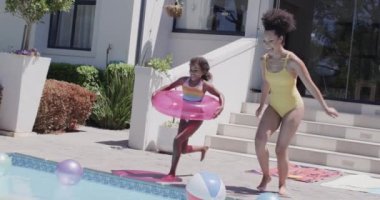 Mutlu Afro-Amerikan anne ve kızı yüzme havuzuna atlıyor, ağır çekimde. Evde, evde ve ailede kaliteli zaman geçirmek.