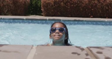 Yüzme havuzunda güneş gözlüğü takan Afrikalı Amerikalı mutlu bir kızın portresi, ağır çekimde. Evde, evde ve çocuklukta kaliteli zaman geçirmek.