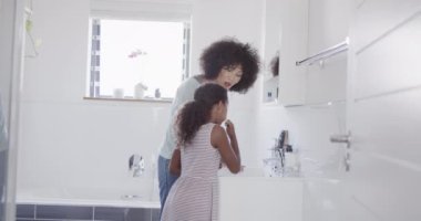 Afro-Amerikan anne ve kızının banyoda dişlerini fırçalaması, ağır çekim. Evde, evde ve ailede kaliteli zaman geçirmek.