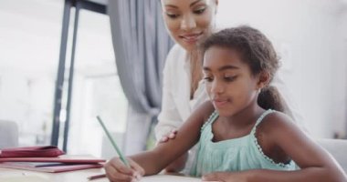 Afrika kökenli Amerikalı anne ve kız oturup birlikte ödev yapıyorlar, ağır çekimde. Evde, evde ve ailede kaliteli zaman geçirmek.