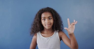 Mutlu Afrikalı Amerikalı kız mavi arka planda işaret dili kullanıyor, ağır çekimde. Çocukluk, sakatlık ve sağırlık.
