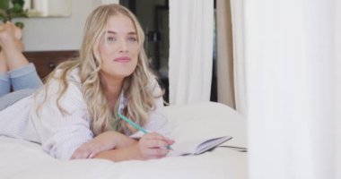 Kafkasyalı mutlu kadın yatakta uzanıyor ve ağır çekimde yazıyor. Yaşam tarzı, evde kaliteli zaman geçirme ve vücut kapsamı.