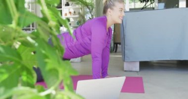 Kafkasyalı mutlu kadın yoga yapıyor ve laptopunu yavaş çekimde kullanıyor. Yaşam tarzı, evde kaliteli zaman geçirme ve vücut kapsamı.