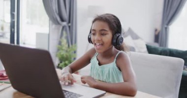 Afrika kökenli Amerikalı kız masada oturuyor, bilgisayarını online ders için kullanıyor, ağır çekimde. Evde kaliteli zaman geçirmek, ev hayatı, eğitim ve çocukluk..