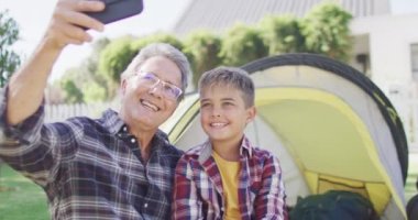 Kafkasyalı büyükbaba ve torun çadırda oturup selfie çekiyorlar, ağır çekimde. Kaliteli zaman geçirme, aile hayatı, aile ve çocukluk.