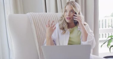 Kafkasyalı mutlu kadın akıllı telefonla konuşuyor ve dizüstü bilgisayarını yavaş çekimde kullanıyor. Yaşam tarzı, evde kaliteli zaman geçirme ve vücut kapsamı.