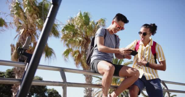 Glad Olika Homosexuella Manliga Par Med Hjälp Smartphone Vid Strandpromenaden — Stockvideo