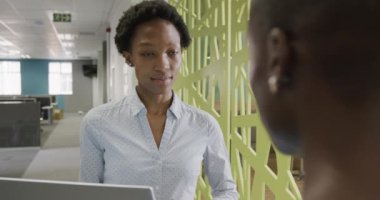 İki Afro-Amerikalı iş kadını iş hakkında konuşuyor ve ofiste dizüstü bilgisayarlarını yavaş çekimde kullanıyorlar. İş, takım çalışması, kapsayıcılık ve iletişim.