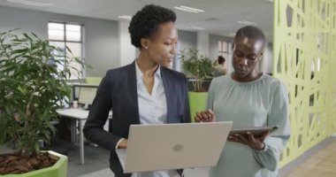 İki Afro-Amerikalı iş kadını ağır çekimde laptoplarını ve tabletlerini kullanarak işi tartışıyor. İş, takım çalışması, kapsayıcılık ve iletişim.
