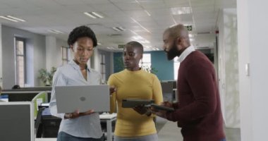 Afrika kökenli Amerikalı iş arkadaşları iş hakkında konuşuyor, ofiste dizüstü bilgisayar ve tablet kullanıyorlar, ağır çekimde. İş, takım çalışması, kapsayıcılık ve iletişim.