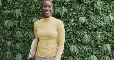 Elinde dizüstü bilgisayar olan, bahçede gülümseyen, ağır çekimde mutlu bir Afro-Amerikan iş kadını portresi. İş, güven ve çalışma.